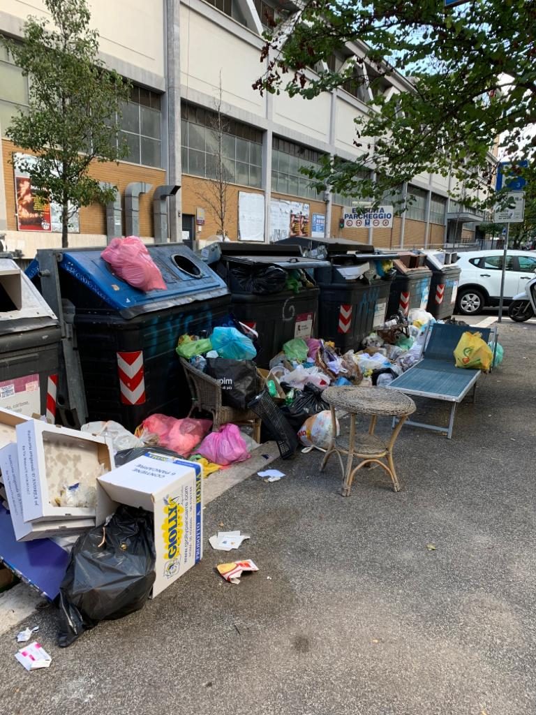I cassonetti colmi di rifiuti, compresi gli ingombranti, di fronte alle sede di Ama in via Dire Daua